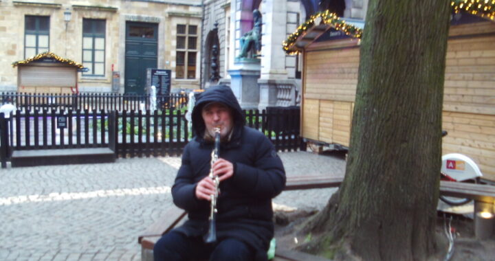 Klarinettist op Hendrik Conscienceplein Antwerpen. Een gedeelte van de kerstmarkt kramen is ook zichtbaar.